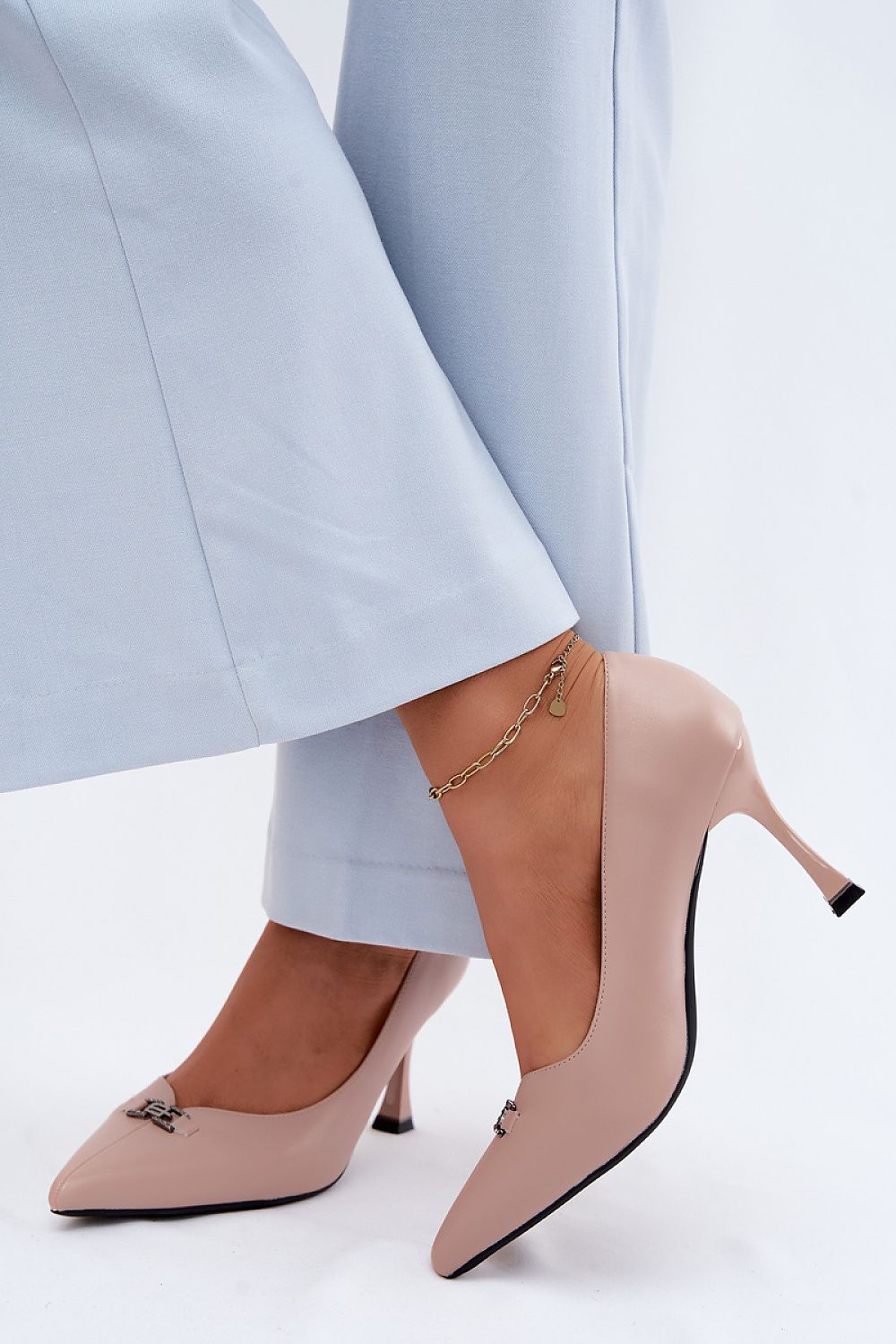 Beige pointed toe heels showcased with light blue pants, featuring a chic pump design and decorative detail.